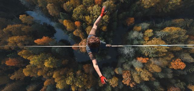 An overhead view of someone walking on a tightrope high above a forest.